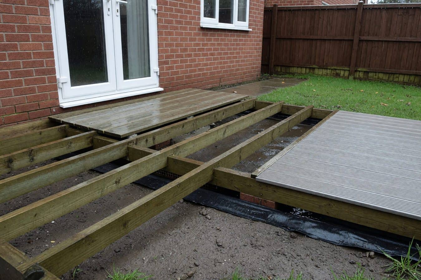 Lifted composite boards revealing wet timber joists and a ventilated void in a Lancashire rear garden