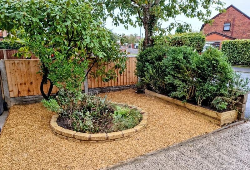 Front garden with golden gravel, circular stone planter, timber raised bed and close-board fencing