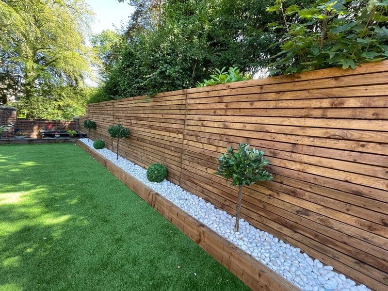 Horizontal timber fence with white gravel border, topiary shrubs and neat green lawn