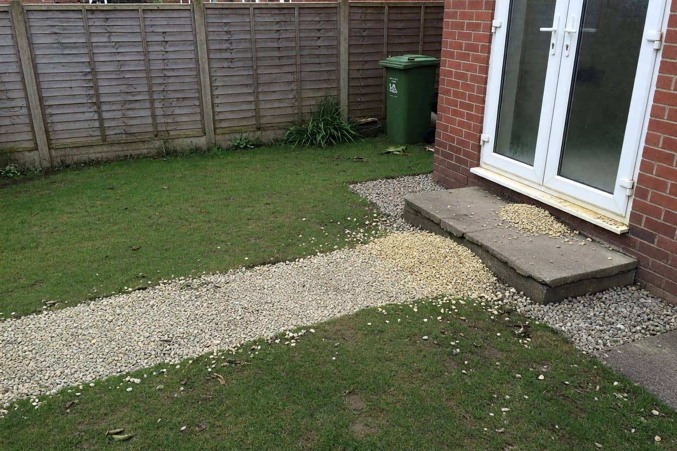 Tired loose-gravel path spilling toward white French doors on a Lancashire rear garden