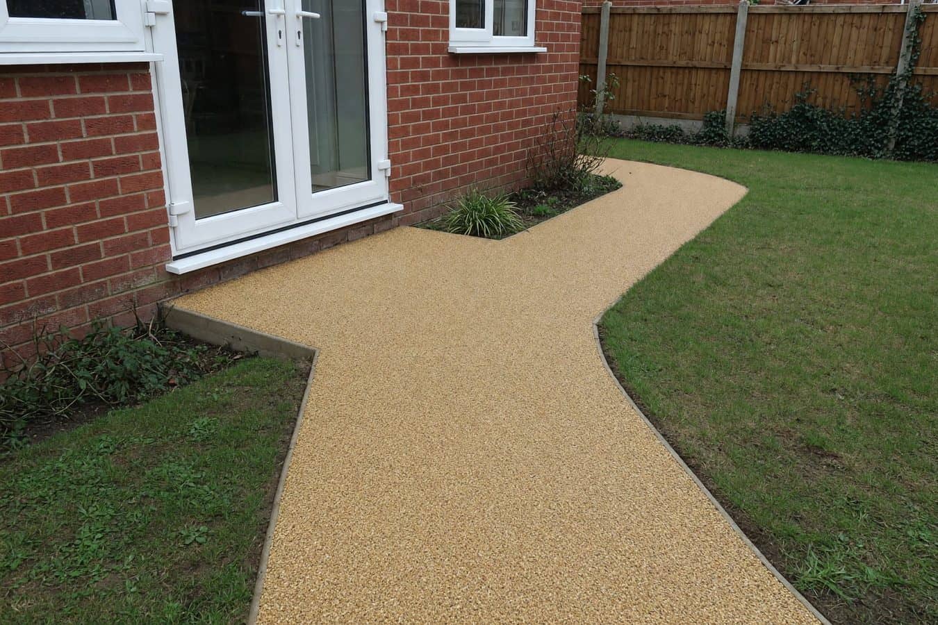 Buff resin bound path meeting a white French-door threshold and falling away from a red-brick Lancashire house