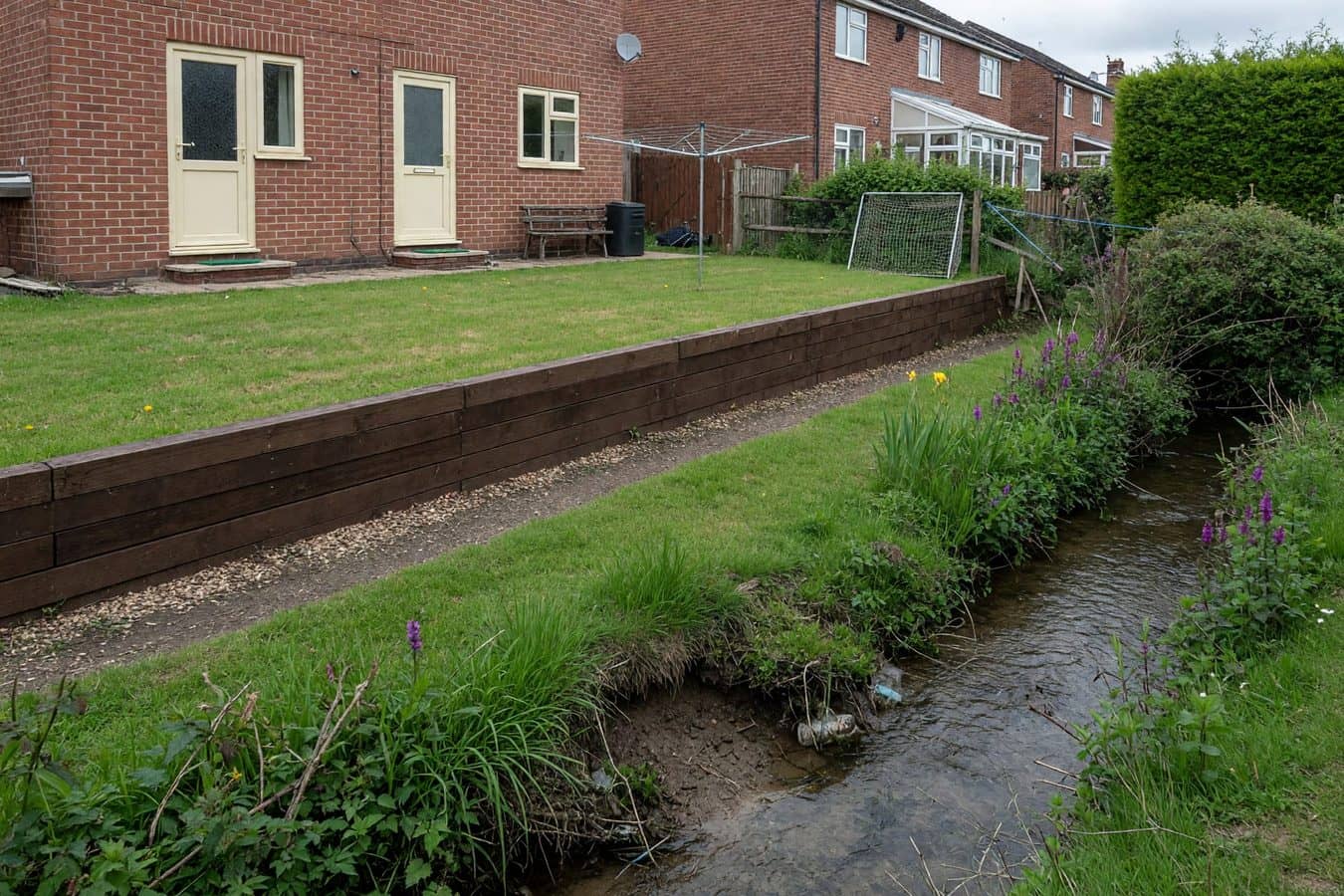 Sound timber sleeper wall set back from a natural garden brook with a planted strip between them