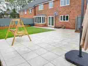A large garden in a new build house with white porcelain paving and artificial grass. Showing the landscaping work of Acorn Gardening