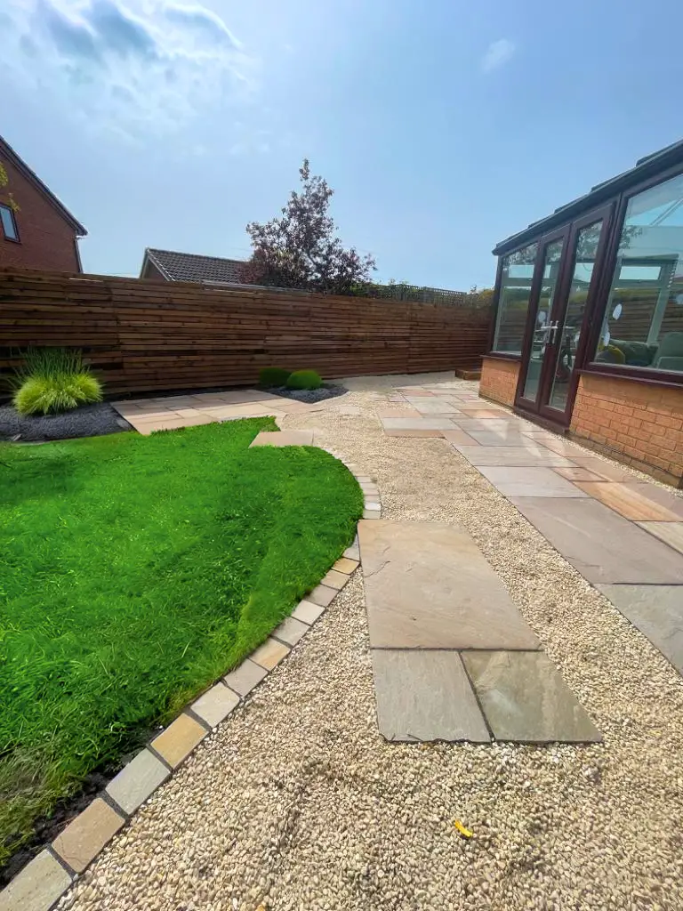 Natural Indian sandstone paving with curved pebble border and lush lawn, meticulously designed and installed by Acorn Landscape Gardening in Preston.
