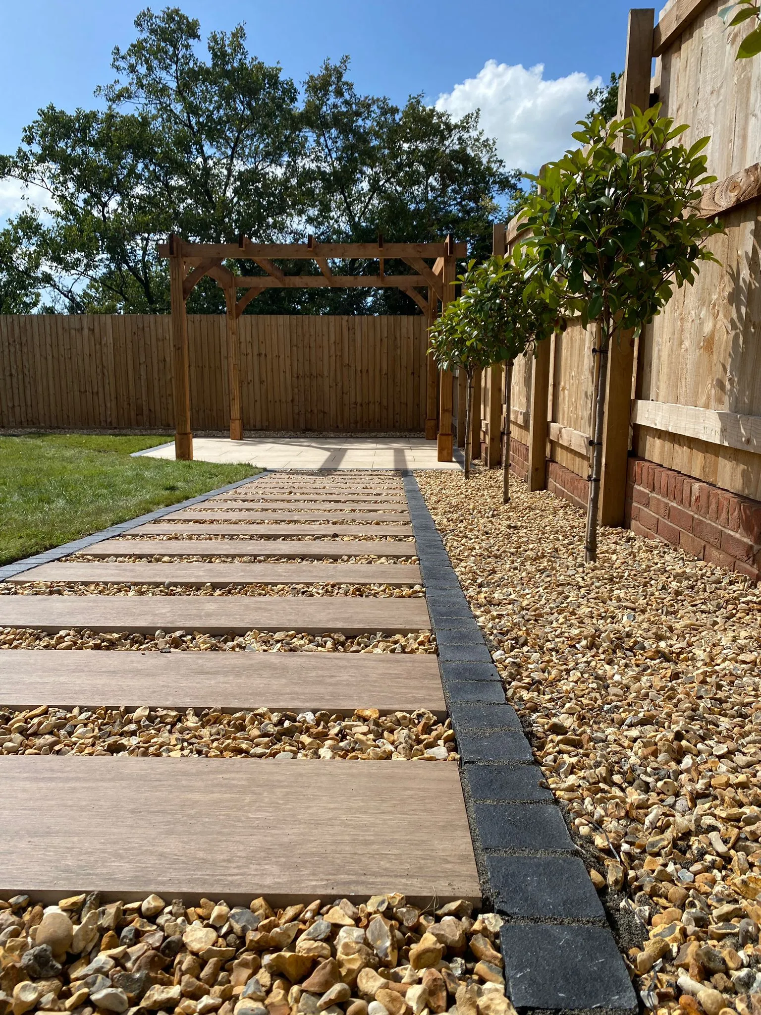 Wood effect porcelain paving with contrasting stone block edging, red robin trees and golden quartz gravel